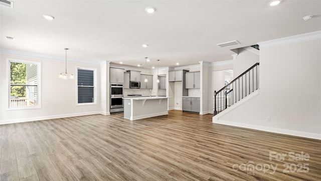 unfurnished living room featuring an inviting chandelier, crown molding, and light hardwood / wood-style flooring