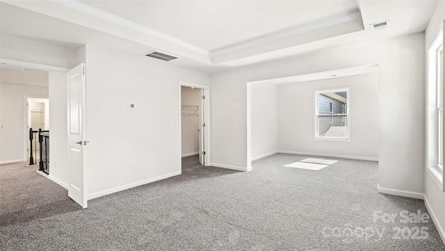 unfurnished bedroom with a spacious closet, a closet, ornamental molding, carpet flooring, and a tray ceiling