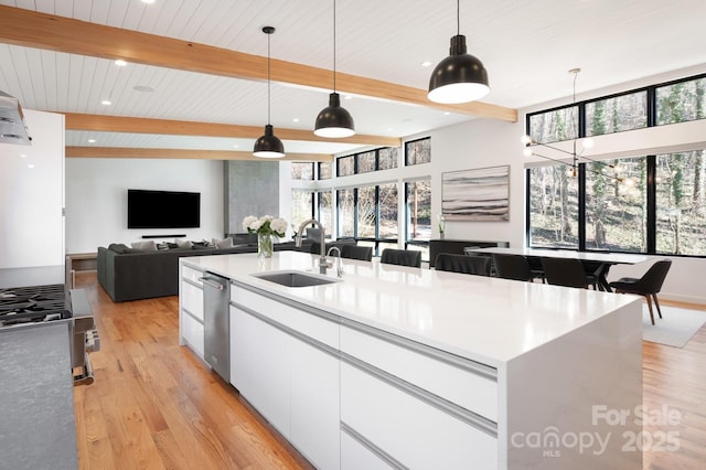 kitchen with sink, white cabinetry, hanging light fixtures, beam ceiling, and a kitchen island with sink