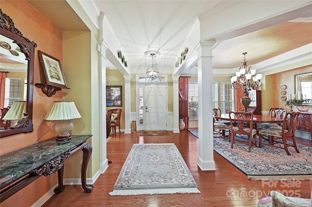 foyer entrance with decorative columns, dark hardwood / wood-style floors, ornamental molding, and a notable chandelier