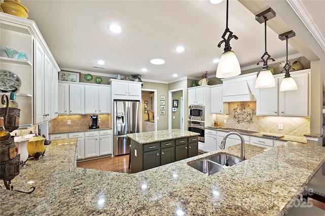 kitchen featuring pendant lighting, appliances with stainless steel finishes, sink, light stone counters, and an island with sink