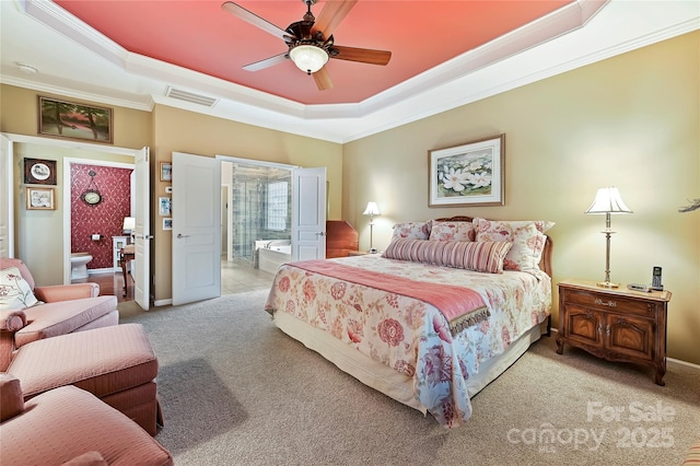 carpeted bedroom with ceiling fan, crown molding, ensuite bathroom, and a raised ceiling