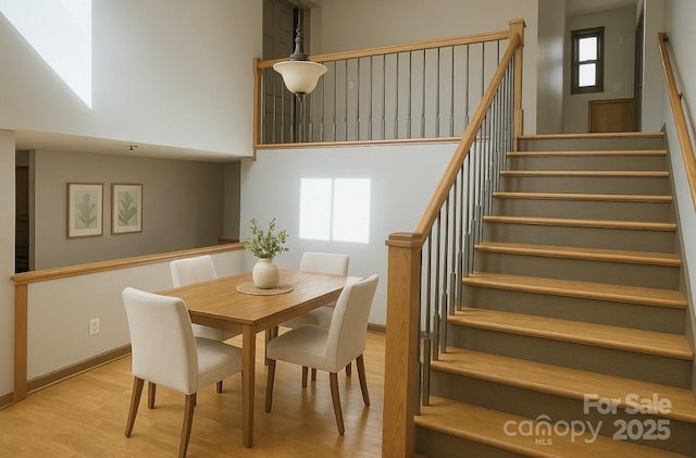 dining room featuring a towering ceiling, wood finished floors, stairs, and baseboards