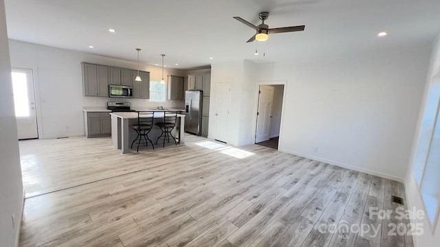 kitchen featuring a breakfast bar area, light wood finished floors, stainless steel appliances, gray cabinetry, and open floor plan