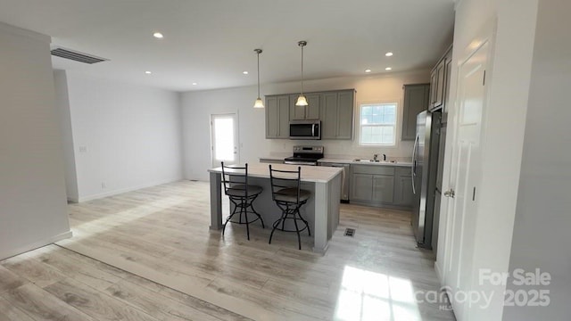 kitchen featuring stainless steel appliances, a kitchen island, visible vents, gray cabinets, and a kitchen bar