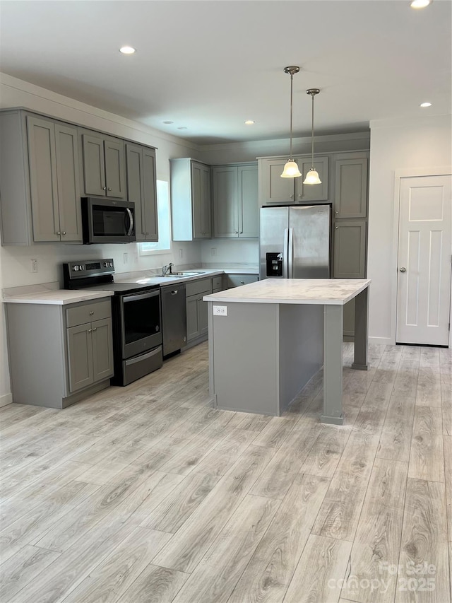 kitchen featuring light wood finished floors, appliances with stainless steel finishes, a center island, gray cabinets, and light countertops