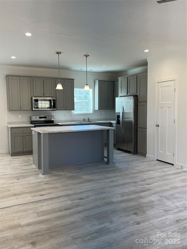 kitchen with a kitchen island, stainless steel appliances, light countertops, gray cabinetry, and light wood-type flooring