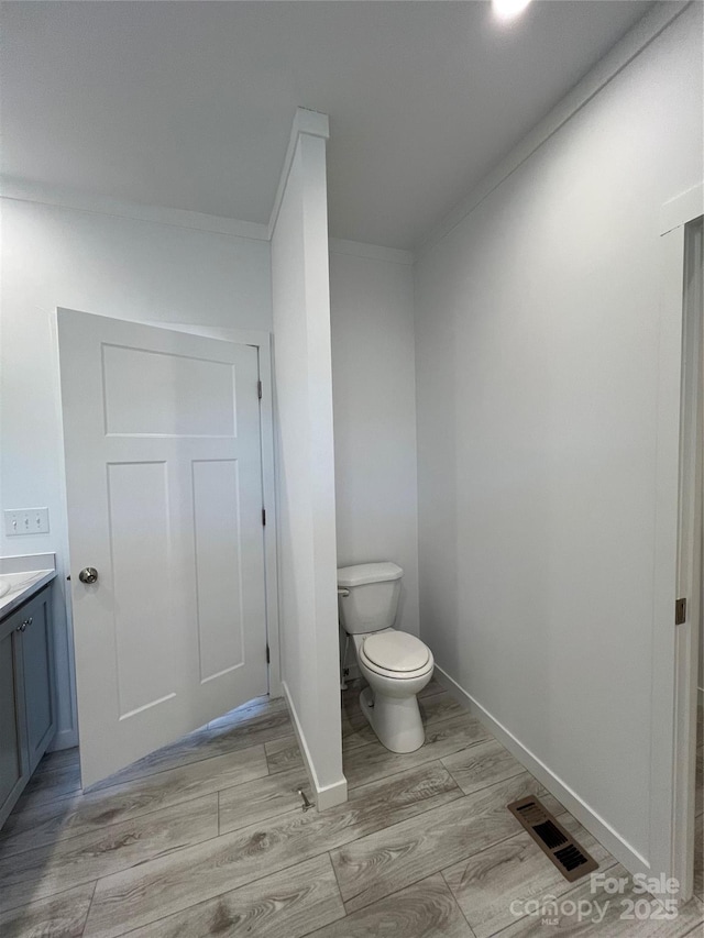 bathroom with toilet, wood finished floors, vanity, visible vents, and baseboards