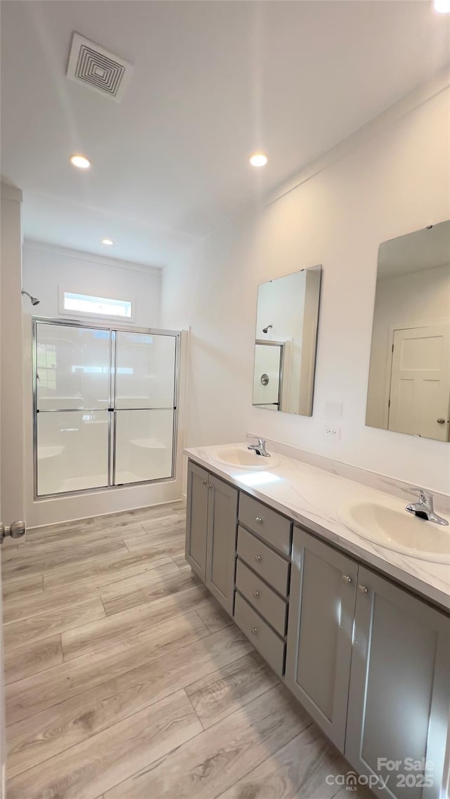 full bathroom featuring a shower with door, visible vents, a sink, and wood finished floors