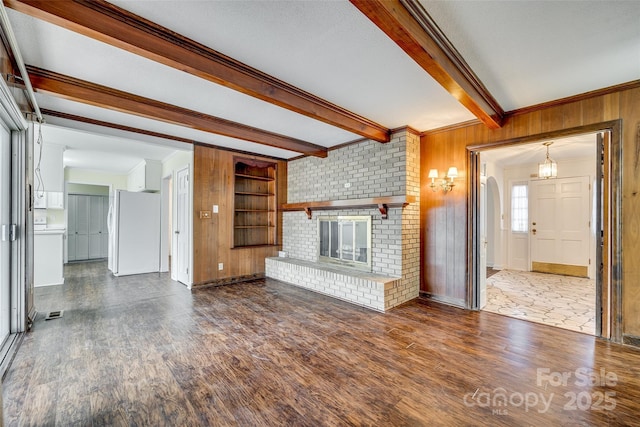 unfurnished living room featuring built in features, a fireplace, dark hardwood / wood-style flooring, beamed ceiling, and wood walls