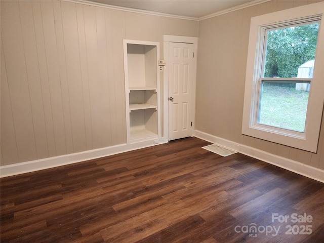 empty room with dark wood-type flooring, built in features, and crown molding