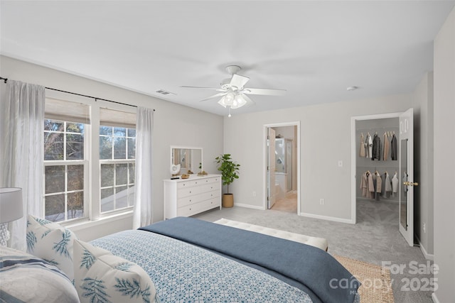 bedroom with ceiling fan, connected bathroom, a walk in closet, light colored carpet, and a closet