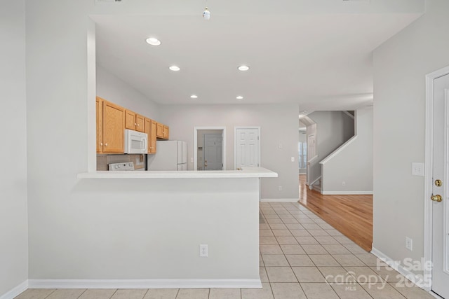 kitchen featuring light tile patterned flooring, white appliances, kitchen peninsula, and light brown cabinets