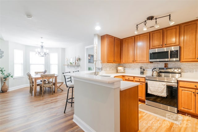 kitchen with kitchen peninsula, sink, decorative light fixtures, light hardwood / wood-style floors, and stainless steel appliances