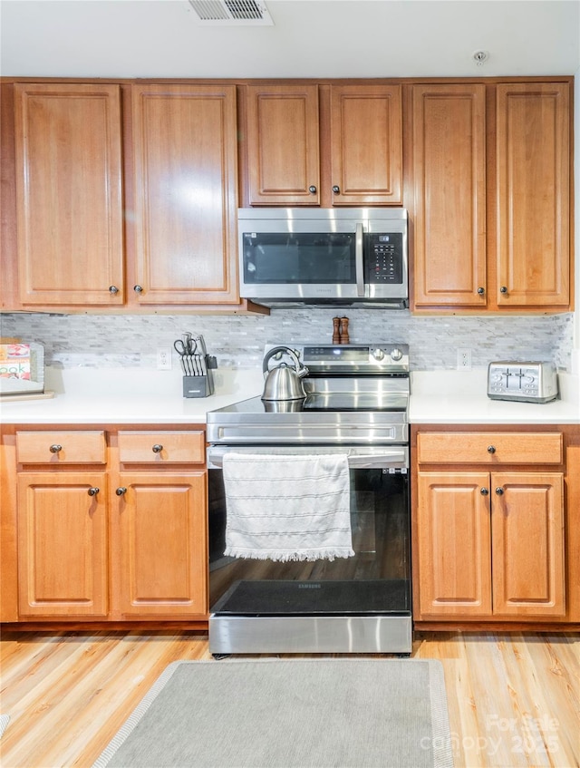 kitchen with light wood-type flooring, stainless steel appliances, and tasteful backsplash