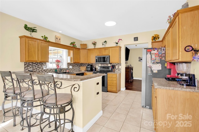 kitchen with a breakfast bar, tasteful backsplash, light tile patterned floors, appliances with stainless steel finishes, and kitchen peninsula