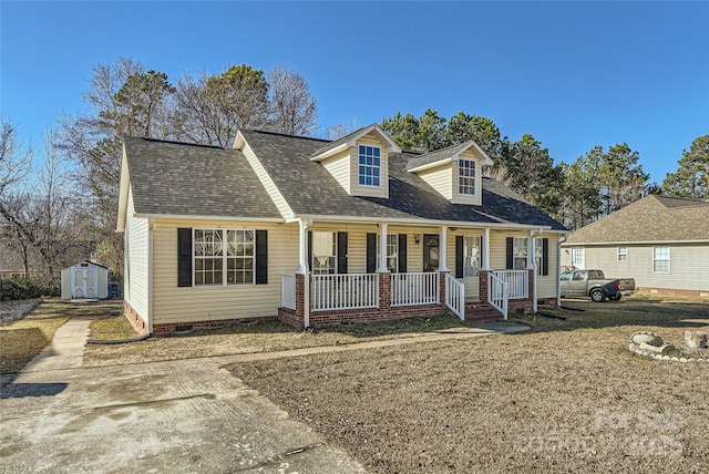 cape cod home featuring covered porch, a front lawn, and a shed