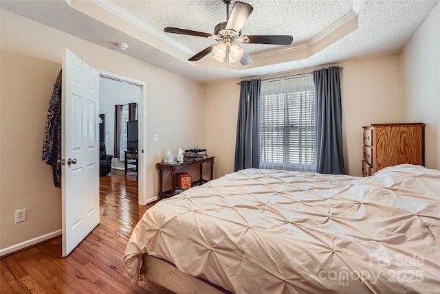 bedroom with crown molding, ceiling fan, a tray ceiling, hardwood / wood-style floors, and a textured ceiling