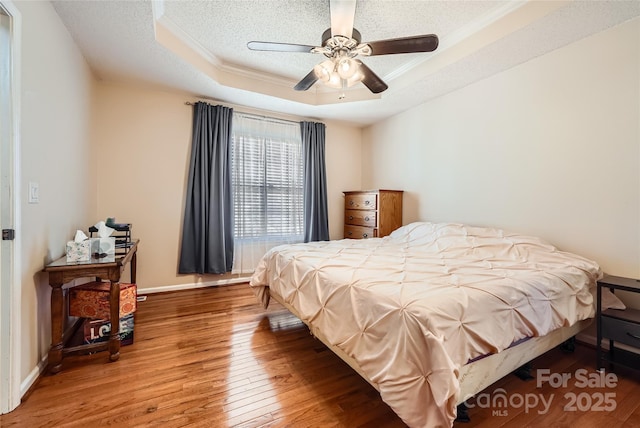 bedroom featuring crown molding, a textured ceiling, wood-type flooring, ceiling fan, and a tray ceiling