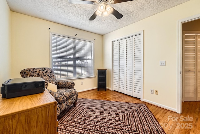 living area featuring light wood-type flooring, a textured ceiling, and ceiling fan