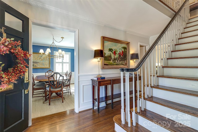 staircase with hardwood / wood-style flooring, crown molding, and an inviting chandelier