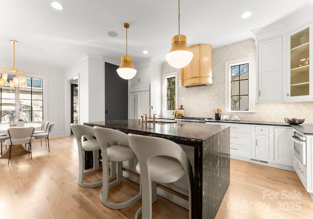 kitchen featuring white cabinetry, premium range hood, hanging light fixtures, and a center island with sink