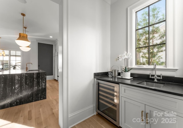 bar featuring wine cooler, sink, hanging light fixtures, and light wood-type flooring