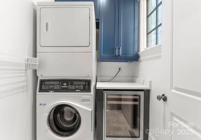 laundry area featuring cabinets, stacked washer and clothes dryer, and beverage cooler