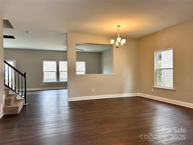 spare room featuring a notable chandelier, dark wood finished floors, stairway, and baseboards