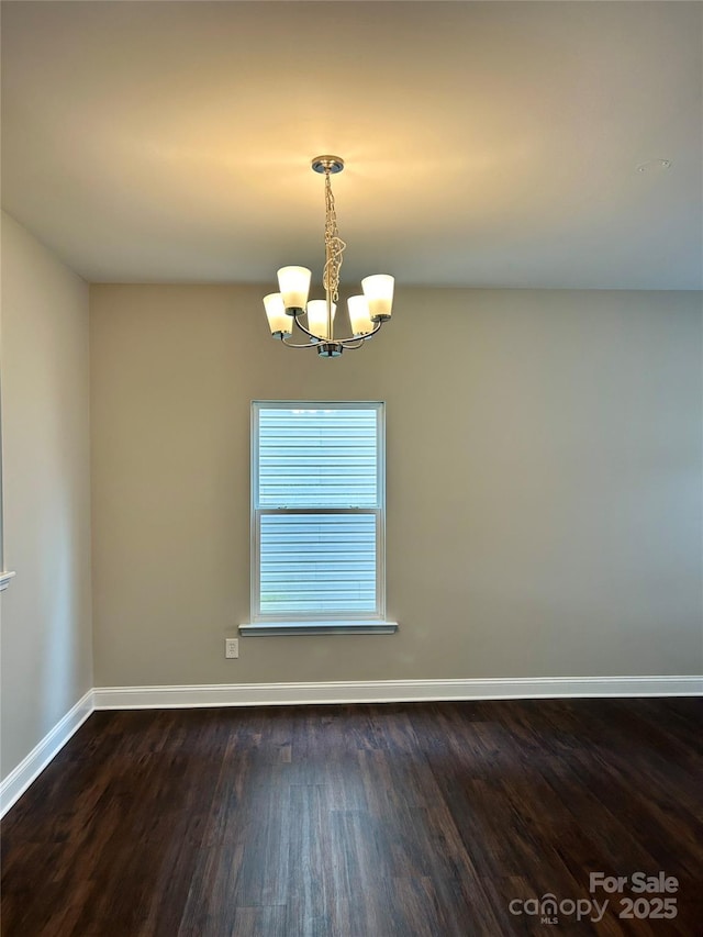 spare room with dark wood-type flooring, a notable chandelier, and baseboards