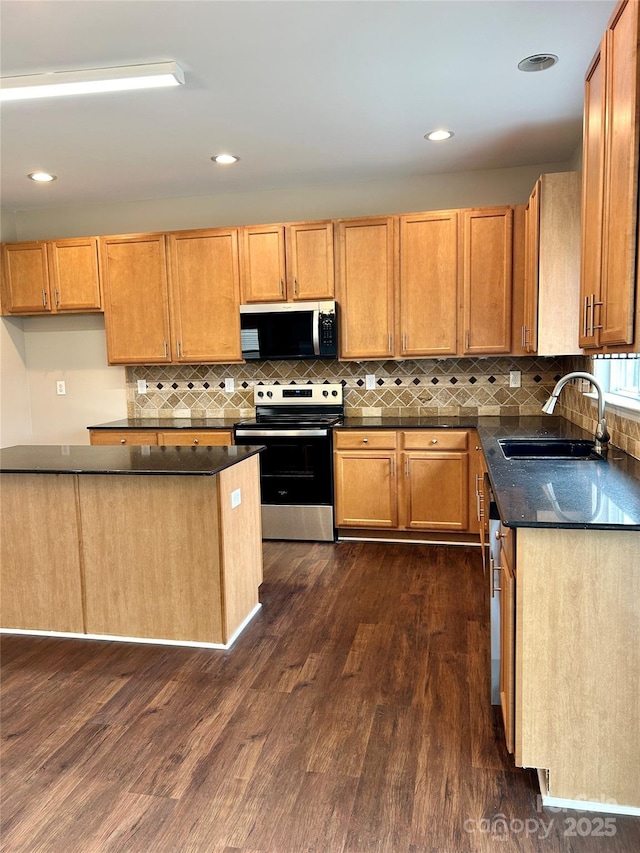 kitchen with appliances with stainless steel finishes, dark countertops, dark wood-style flooring, and a sink