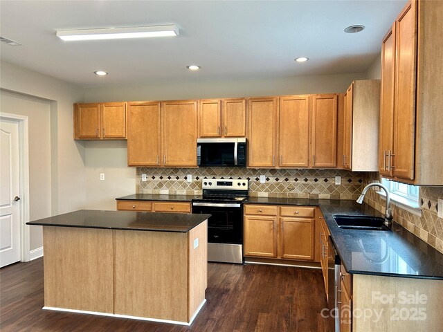 kitchen with dark countertops, a kitchen island, dark wood-style flooring, stainless steel appliances, and a sink