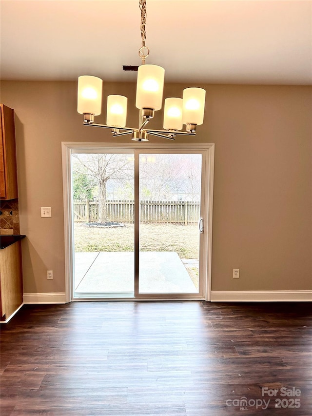 unfurnished dining area featuring baseboards, a chandelier, and dark wood-type flooring