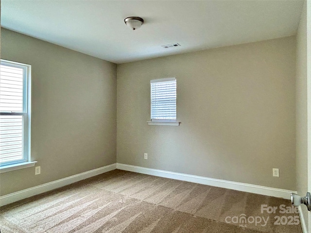 carpeted spare room with a wealth of natural light, visible vents, and baseboards