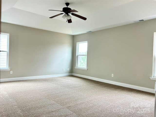 carpeted empty room with a tray ceiling, visible vents, and baseboards