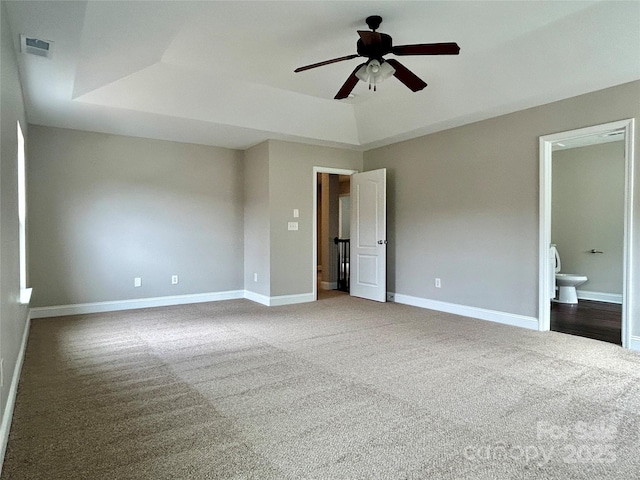 unfurnished bedroom featuring carpet floors, a tray ceiling, visible vents, and baseboards