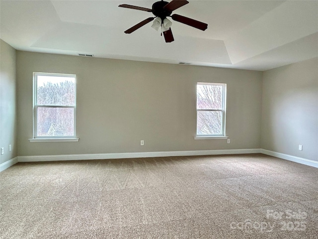 unfurnished room with light colored carpet, a ceiling fan, visible vents, baseboards, and a tray ceiling