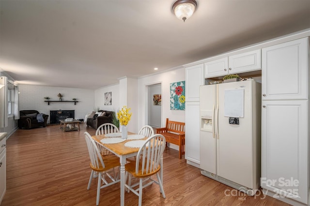 dining area featuring a fireplace, ornamental molding, brick wall, and light hardwood / wood-style flooring