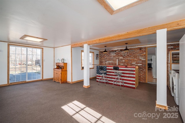 unfurnished living room with dark carpet, washing machine and dryer, beamed ceiling, and brick wall