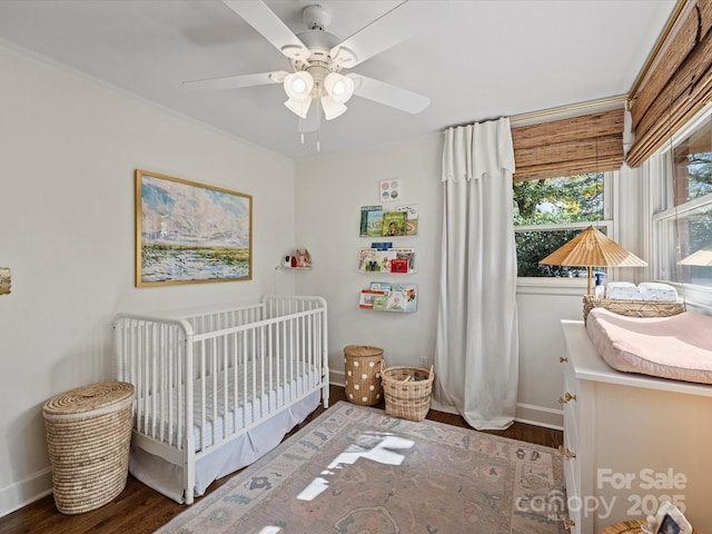 bedroom with ceiling fan, a nursery area, and dark hardwood / wood-style floors