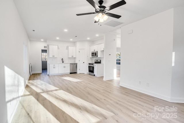 unfurnished living room with light wood-type flooring, ceiling fan, a healthy amount of sunlight, and sink