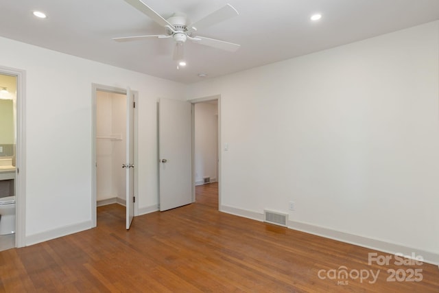 unfurnished bedroom with ceiling fan, a walk in closet, wood-type flooring, and connected bathroom