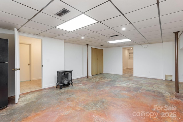 basement featuring a drop ceiling, black refrigerator, and a wood stove