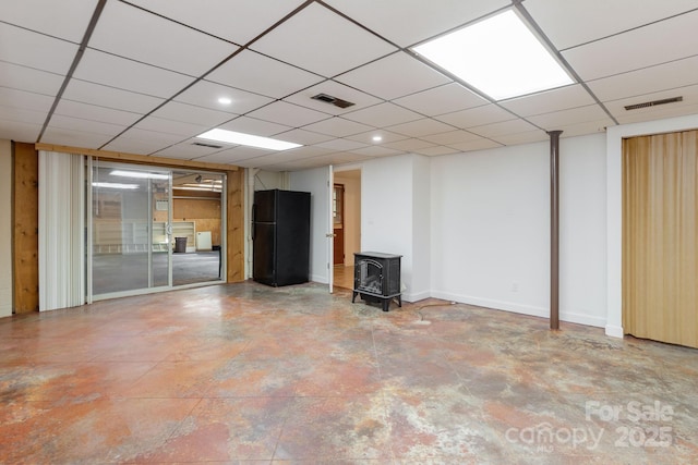 basement featuring black refrigerator, a paneled ceiling, and a wood stove