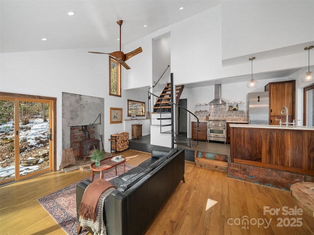 living room featuring ceiling fan, sink, light wood-type flooring, a wood stove, and high vaulted ceiling