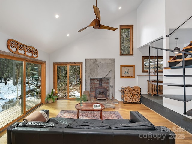 living room featuring ceiling fan, high vaulted ceiling, a wood stove, and hardwood / wood-style flooring