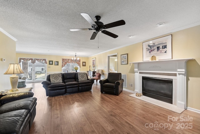 living room featuring hardwood / wood-style flooring, ornamental molding, ceiling fan with notable chandelier, and a textured ceiling