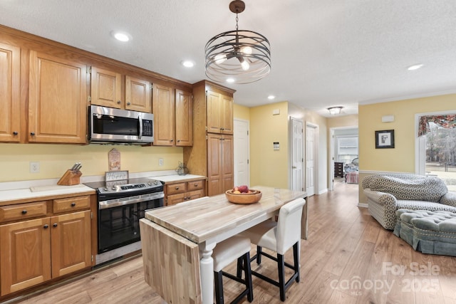 kitchen with decorative light fixtures, light hardwood / wood-style flooring, a center island, and appliances with stainless steel finishes