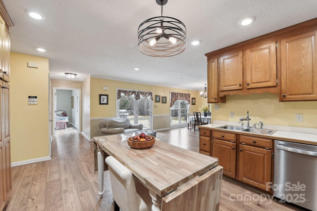 kitchen with pendant lighting, sink, wooden counters, a kitchen island, and stainless steel dishwasher