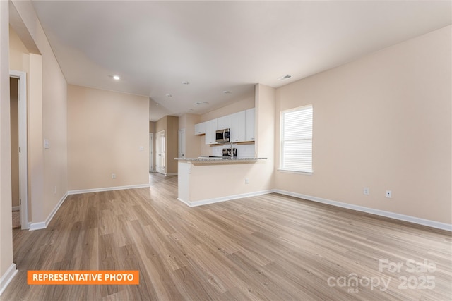 unfurnished living room with baseboards, recessed lighting, and light wood-style floors